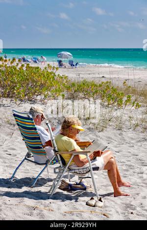 Seniorenpaar, das am Strand in Siesta Key, Sarasota, an der West- oder Golfküste von Florida, USA, liest. Stockfoto