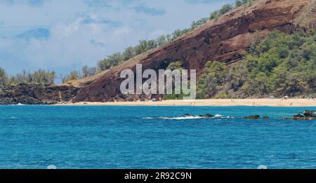 Sandstrand vor einem großen Lavafelsen mit tiefblauem Meer, wenige Urlauber baden am goldenen Sandstrand, USA, Hawaii, Maui, Kihei Stockfoto
