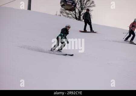 Ein junger Mann mit Skibrille und Winterkleidung fährt mit einem Paar Skiern auf einer schneebedeckten Berghänge Stockfoto