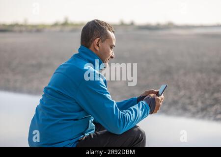 Junger Latino-Mann in Sportbekleidung schaut auf sein Handy. Stockfoto