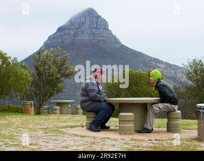 Berge, Menschen und entspannen Sie sich am Tisch, auf der Bank oder in der Natur, wandern und Wanderer, die sich mit Blick, Landschaft und natürlicher Schönheit unterhalten. Outdoor, Berge und Stockfoto