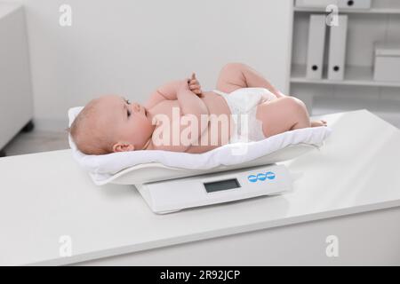 Niedliches kleines Baby, das in der Klinik auf einer Waage liegt Stockfoto