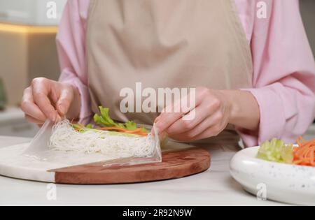 Leckere Frühlingsrollen. Frau, die Zutaten in Reispapier einwickelt, am weißen Tisch, Nahaufnahme Stockfoto