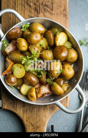 Kleine Kartoffeln, Speck, Petersilie auf einer Pfanne auf Holzhintergrund, Nahaufnahme Stockfoto