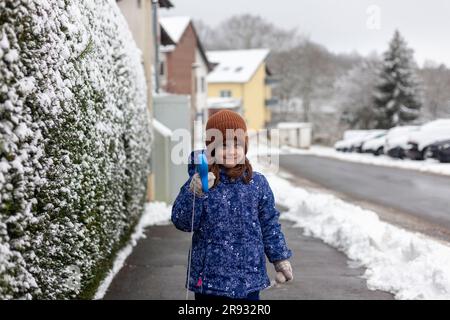 Süßes kleines Mädchen mit Hundeleine, während es auf einer verschneiten Straße steht Stockfoto