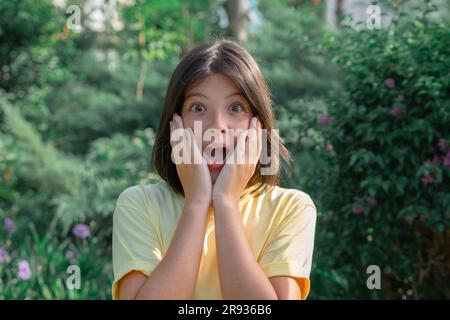 Verängstigtes junges Mädchen mit weit geöffneten Augen. Das Mädchen bedeckte ihr Gesicht mit den Händen, während es ihren Mund weit öffnete. Stockfoto