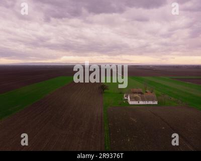 Luftflug über Winterlandwirtschaftsfelder mit verlassener Ranch bei Sonnenuntergang. Vojvodina, Serbien, Europa. Stockfoto