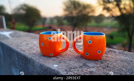 Zwei leere orangefarbene Keramikkaffee- oder -Teetassen auf dem Dach mit Naturhintergrund. Stockfoto