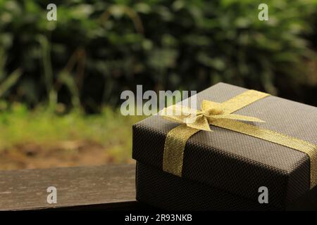 Verschiedene Geschenkschachteln mit Sonnenlicht auf dem Rasen des Parks an einem sonnigen Sommertag:Schachtel für Geschenk mit goldenem Band auf dem Holztisch Stockfoto