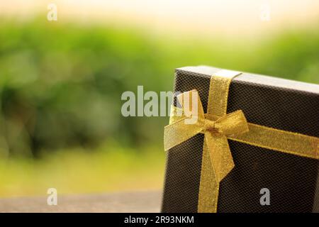Verschiedene Geschenkschachteln mit Sonnenlicht auf dem Rasen des Parks an einem sonnigen Sommertag:Schachtel für Geschenk mit goldenem Band auf dem Holztisch Stockfoto