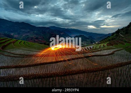 Brennende Stahlwolle, die sich dreht. Bei Sonnenaufgang glühende Funken von rotierender Stahlwolle auf dem Terrassenfeld in Mu Cang Chai, Provinz Yen Bai, Vietnam Stockfoto