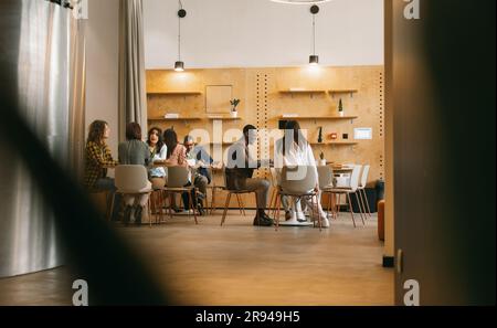 Eine generationenübergreifende, multikulturelle Gruppe kreativer Menschen, die ein neues Geschäftsprojekt starten. Sie arbeiten im Café des modernen CO-Arbeitsbereichs Stockfoto