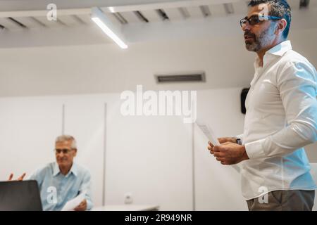 Eine Seitenansicht von einem gutaussehenden männlichen Geschäftsmann, der eine Rede im Klassenzimmer hält. Er präsentiert neue Geschäftsideen Stockfoto