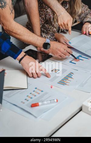 Nahaufnahme von Geschäftsleuten, die monatliche Gewinnberichte im Büro durchsehen. Arme, die auf Dokumente zeigen. Zugeschnittenes Foto Stockfoto