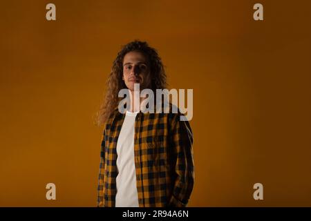 Ein stilvoller Hipster mit langen Locken, weißem T-Shirt und gelb-schwarzem Hemd. Studioaufnahmen Stockfoto