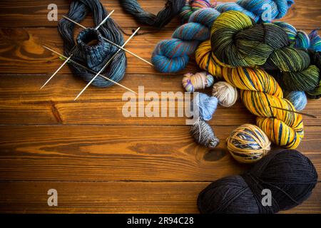 Farbige Fäden, Stricknadeln und andere Handstrickgegenstände auf einem dunklen Holztisch. Stockfoto