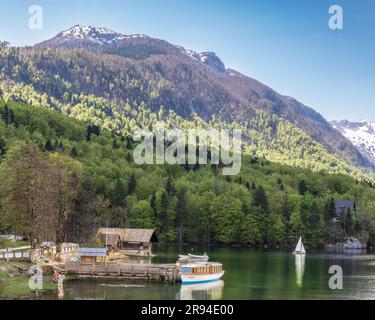 Ruhige Szene am Bohinjsee, Triglav-Nationalpark, Oberkarniola, Slowenien. Das Tourboot liegt am Anlegesteg. Segelboot in der Ferne. Stockfoto