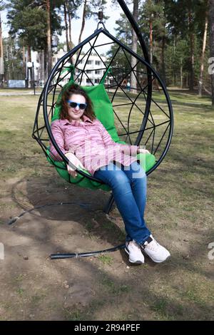 Frau, die sich im Park auf einem Hängestuhl im Freien entspannt Stockfoto
