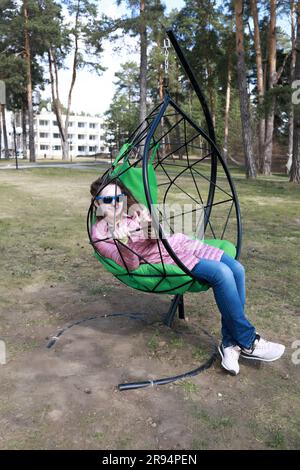 Eine Frau, die im Park auf einem Stuhl im Freien sitzt Stockfoto