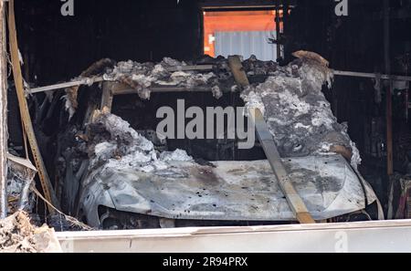 Jarmen, Deutschland. 24. Juni 2023. Ein abgebranntes Auto steht in einer Garage an den Feuerruinen eines Familienhauses in Jarmen. Bei dem Brand des Wohnungsgebäudes in Jarmen (Bezirk Vorpommern-Greifswald) starben am Samstag zwei Menschen. Als die Einsatzkräfte der Polizei und der Feuerwehr eintrafen, war das Gebäude bereits vollständig in Flammen, wie die Polizei ankündigte. Ob die Toten die Hausbesitzer waren, ein 60-jähriger Mann und seine 59-jährige Frau, war immer noch unbekannt. Am Samstag konnte die Polizei noch keine Informationen über die Brandursache geben. Kredit: Stefan Sauer/dpa/Alamy Live News Stockfoto