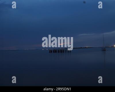 Dunkler Himmel in der Dämmerung entlang einer Barnegat Bay, New Jersey Dock. Fernlichter säumen das Ufergebiet. Stockfoto