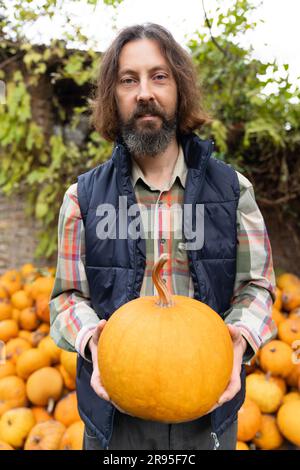 Bärtiger Bauer mit Kürbis auf einem Haufen Kürbisse. Stockfoto