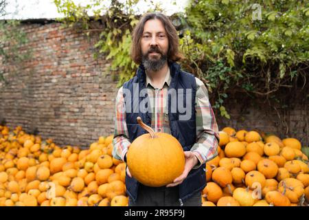 Bärtiger Bauer mit Kürbis auf einem Haufen Kürbisse. Stockfoto