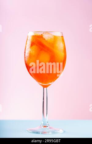 Aperol Spritz Cocktail in Glas auf pinkblauem Hintergrund. Cocktail Aperol Spritz mit Orange und Eiswürfeln. Schließen Stockfoto