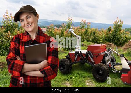 Der Bauer steuert den autonomen Roboter in einem Obstgarten. Konzept der intelligenten Landwirtschaft. Stockfoto