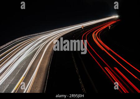 Abstraktes Bild von Nachtverkehrsampeln auf der Straße. Autolichtwanderungen bei Nacht auf kurvigen Asphaltstraßen. Lange Belichtung, bei der die Bewegung der Fahrzeuge von angezeigt wird Stockfoto