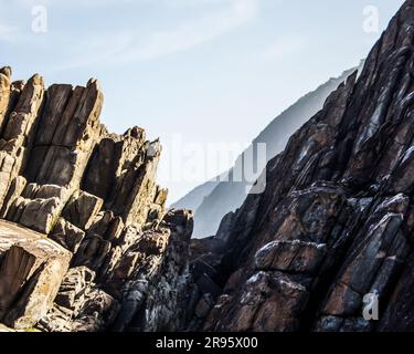 Gekippte Felsschichten der Tsitsikamma-Küste, Südafrika, mit den entfernten blauen Klippen im Hintergrund. Stockfoto