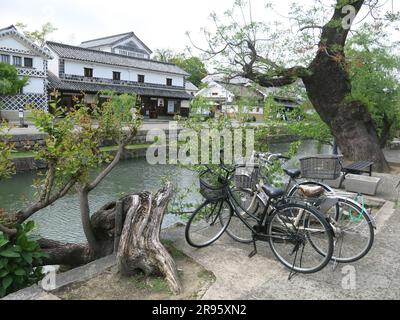 Kurashiki verfügt über eine gut erhaltene Kanalgegend mit den alten Reislagerhäusern, die weiß mit schwarzen Fliesen gestrichen sind, und weinenden Weiden am Ufer. Stockfoto