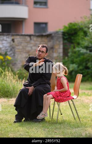 Ein Priester, der einem kleinen Kind während der Beichte Absolution erteilt. Das Kind bereitet sich auf die erste Heilige Kommunion vor. Stockfoto