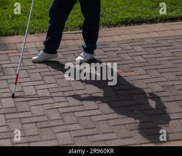 Eine gesichtslose blinde schwangere Frau läuft mit einem Stock die Straße entlang. Stockfoto