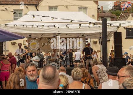 Leigh on Sea, Großbritannien. Juni 2023. In der Altstadt von Leigh-on-Sea trifft sich eine lebhafte Menschenmenge, während die Danny Greene Band unter einem weißen Baldachin vor dem Crooked Billet Pub auftritt. Das Open-Air-Konzert bietet E-Gitarren, Schlagzeug und Gesang, die das lokale Publikum während einer Community-Musik-Veranstaltung anregen. Eine Band unterhält Leute bei einem Drink im Crooked Billet. Die Leute draußen in Old Leigh auf dem Meer genießen das heiße Wetter. Penelope Barritt/Alamy Live News Stockfoto
