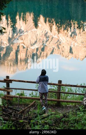 Junge Frau, die den Blick auf den Karersee (Carrezza-See) genießt, während sich die Latemar-Gebirgskette im See spiegelt. Reisen Nach Italien. Wanderkonzept. Stockfoto