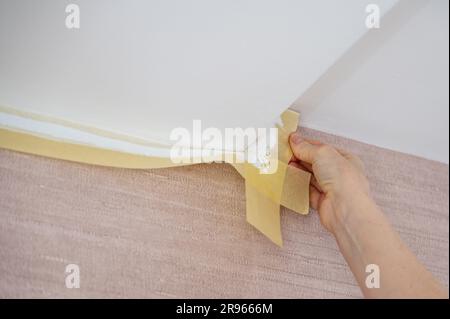 Entfernen des Abdeckbands nach dem Lackieren der Decke in einem Raum Stockfoto