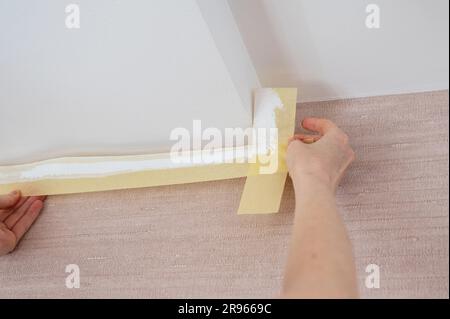 Entfernen des Abdeckbands nach dem Lackieren der Decke in einem Raum Stockfoto