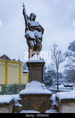 Klodzko, Polen - Januar 2023: Kleine alte Statue an der Seite der gotischen Brücke über den Fluss Mlynowka, die im Winter von Schnee bedeckt ist Stockfoto