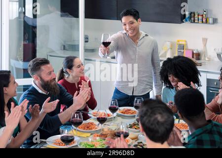 Junge Freunde stoßen zusammen an, um den jungen asiatischen Mann zu feiern, Freunde trinken Wein und essen italienisches Essen Stockfoto