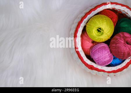 Garne zum Häkeln. Mehrere mehrfarbige Wollfäden im Korb auf weißem, flauschigem Hintergrund. Draufsicht, Webbanner mit Kopierbereich. Co Stockfoto