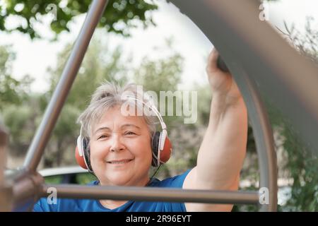 Aktive, fettleibige ältere Frau in Sportbekleidung trainiert auf einem Parktraininggerät, während sie Musik über ihre Kopfhörer hört Stockfoto