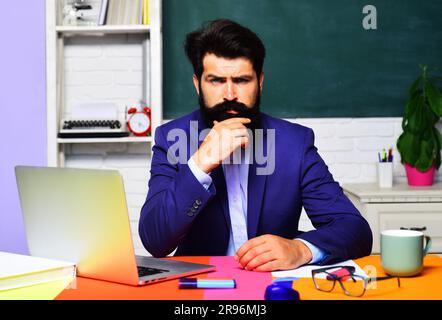 Lehrerjob. Ein bärtiger Lehrer im Klassenzimmer. Lernen und Bildung. Professioneller Lehrer oder Universitätsprofessor, der mit ihm am Tisch sitzt Stockfoto