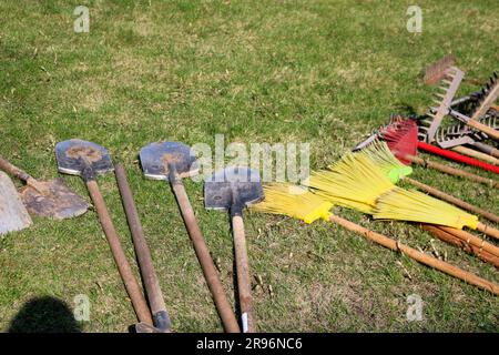 Viele Rechen, Schaufeln und Bürsten zum Reinigen des Gebiets liegen auf dem grünen Gras Stockfoto