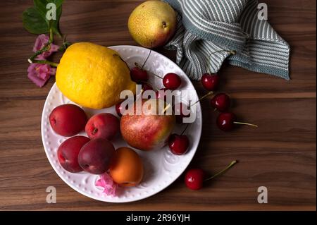 Frische Aprikosen, Zitronen, Birnen und süße Kirschen auf dem weißen Teller Stockfoto