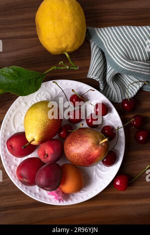Frische Aprikosen, Zitronen, Birnen und süße Kirschen auf dem weißen Teller Stockfoto
