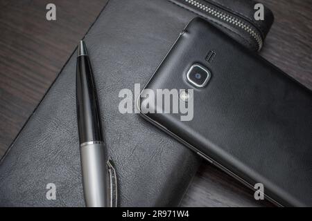 Telefon mit Stift und Handtasche liegen auf einem Holztisch Stockfoto