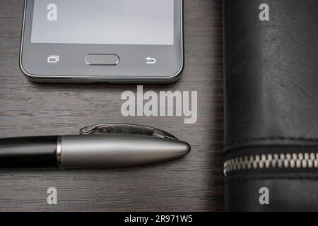 Telefon mit Stift und Handtasche liegen auf einem Holztisch Stockfoto