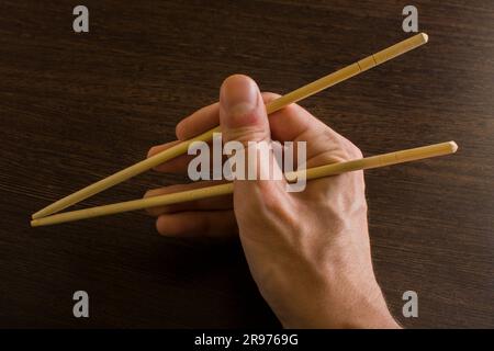 Stäbchen in der rechten Hand auf einem Hintergrund aus braunem Holz Stockfoto