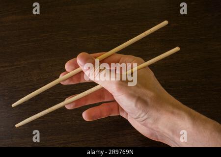 Stäbchen in der rechten Hand auf einem Hintergrund aus braunem Holz Stockfoto